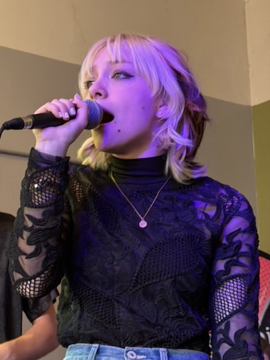 Joanna singing into a microphone, a purple light shines on her face
